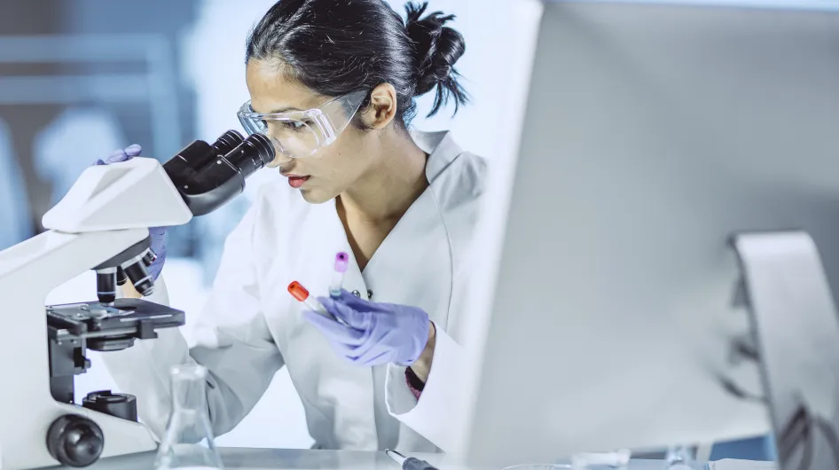 A young woman doctor looks into a microscope while conducting clinical research